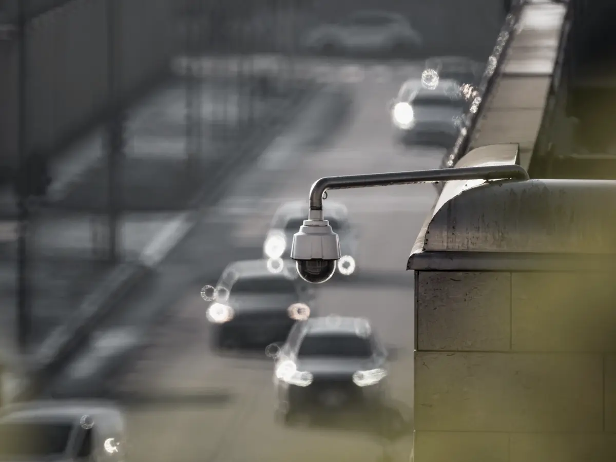 A dome camera mounted above a road, traffic out of focus behind it