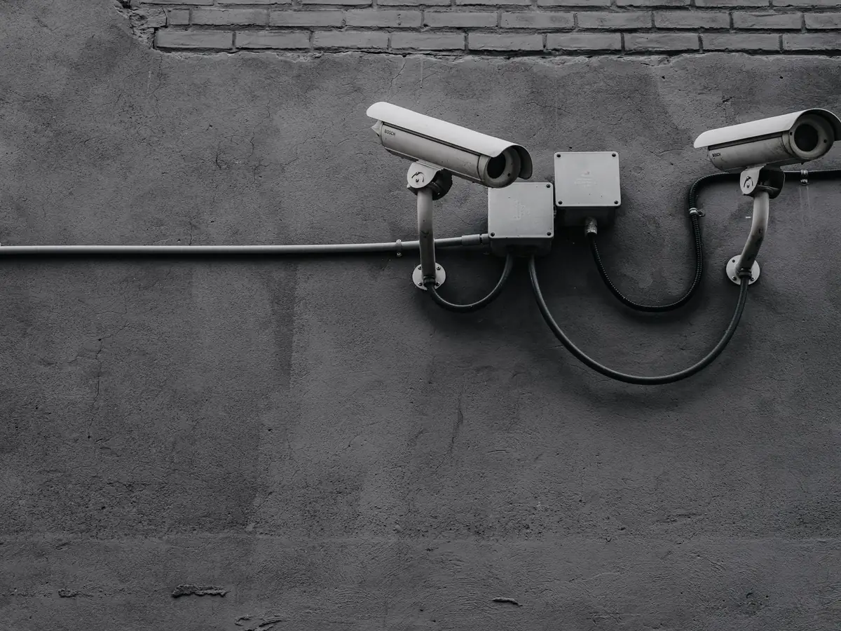 Two bullet cameras on a bracket against a bare concrete wall