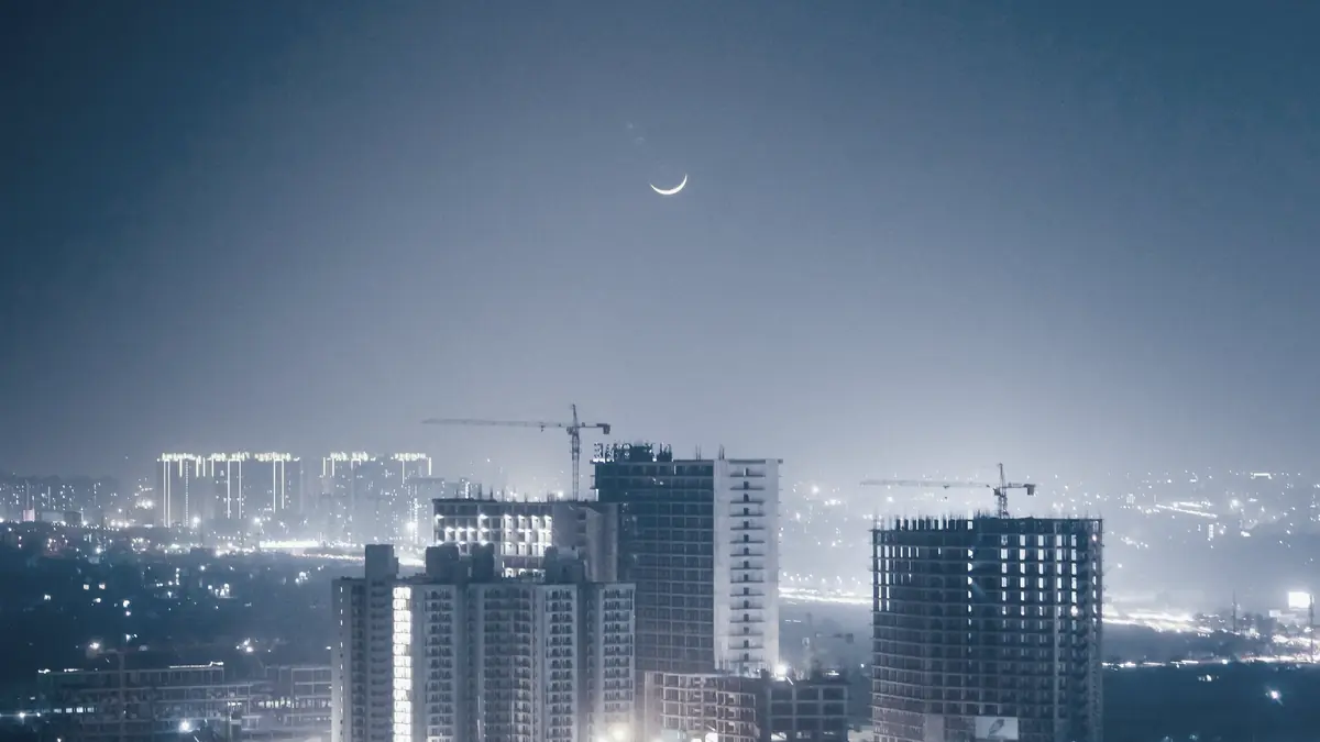 Gurugram after dark: towers and tower cranes under a thin crescent moon