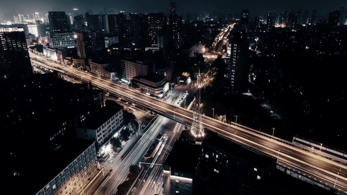 A multi-level road interchange at night, traffic drawn out into light trails