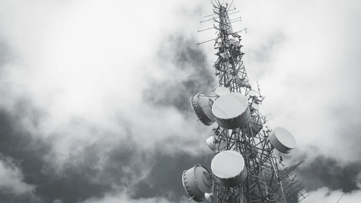 Microwave dishes on a lattice communications tower, half lost in fog