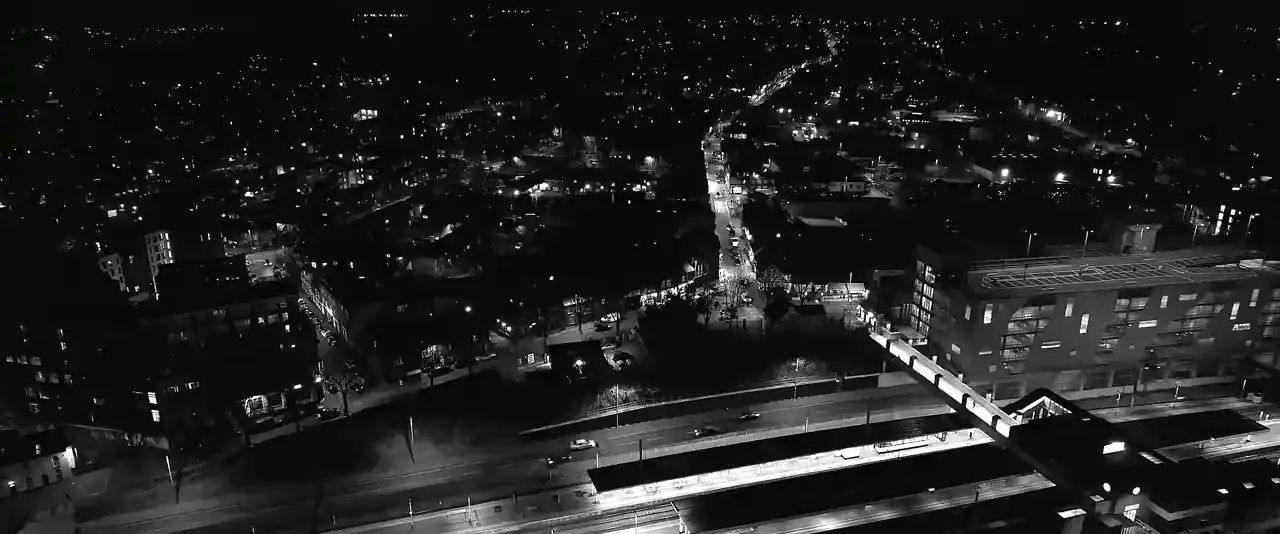 A slow aerial drift over a city at night, roads and rail lines picked out in light