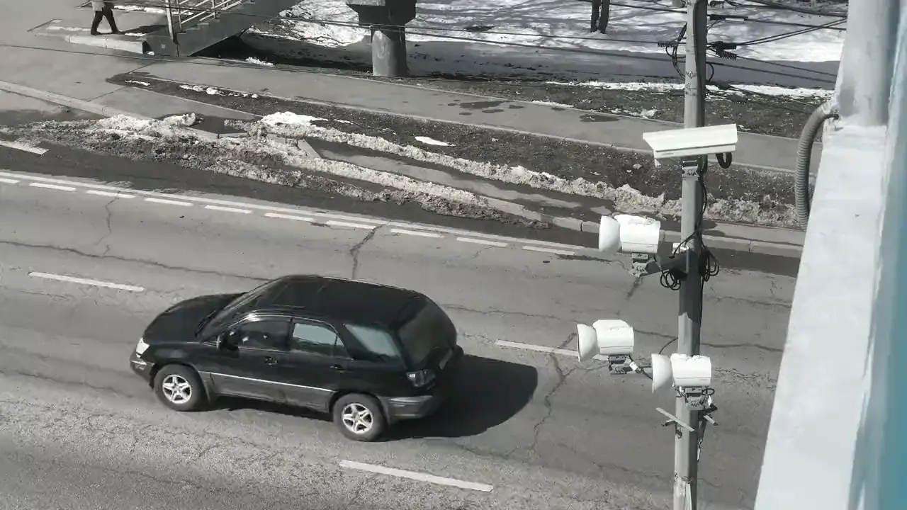 Traffic cameras on a roadside pole as a bus and cars pass beneath